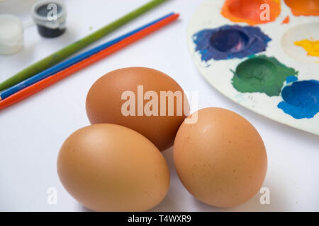 Trois œufs de Pâques faire revenir le poulet, avec des peintures colorées floues, palette sur l'arrière-plan, l'équipement de peinture sur fond blanc, œufs de Pâques Banque D'Images