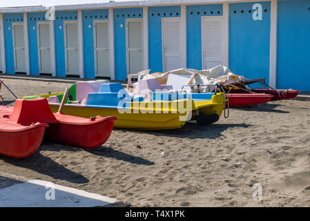 Bateaux colorés sur la plage de sable d'un établissement de bord de plage, avec cabines à l'arrière-plan blanc Banque D'Images