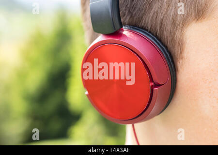 Casque rouge sur la tête d'un adolescent sur un fond de vert des conifères dans le parc. L'électronique moderne pour se détendre et se détendre Banque D'Images