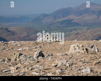 Un cairn sur Helvellyn dans le Lake District en Cumbrie, Angleterre, RU entouré de sol rocheux sur une journée ensoleillée, avec des collines en arrière-plan Banque D'Images