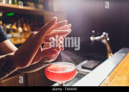 Les mains de barman en saupoudrant l de jus dans le verre à cocktail rempli de boisson alcoolisée sur le fond sombre. Banque D'Images