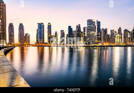 Vue imprenable sur la skyline de Dubaï illuminée pendant le coucher du soleil les bâtiments et gratte-ciel reflété sur un écoulement d'eau douce à l'avant-plan. Banque D'Images