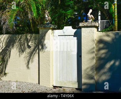 Une porte en bois avec des pélicans en pierre au sommet de chaque pilier, avec une belle à l'intérieur d'un quartier résidentiel tropical entourant une cour intérieure Boca Grande, FL Banque D'Images