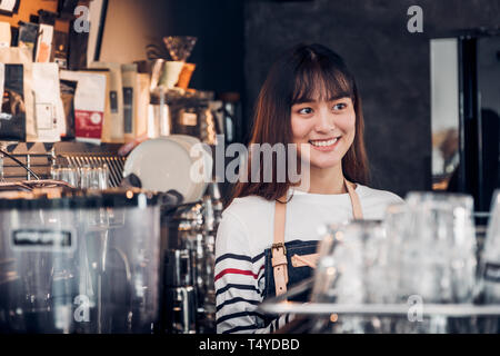 Asian female barista de porter un tablier jean au comptoir bar avec smile face, cafe service concept, propriétaire démarrage d'entreprise. Banque D'Images