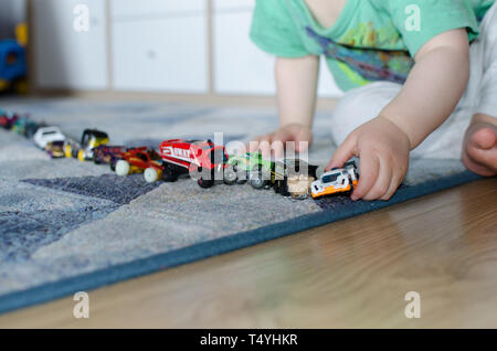 La queue de l'enfant jouets sur le plancher à la maison. Kid alignant voitures de jouet sur le plancher. Banque D'Images