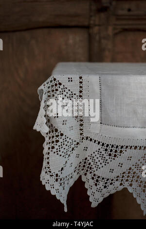 Un gros plan d'une nappe en dentelle blanche taillé sur une table contre un mur lambrissé de bois Banque D'Images