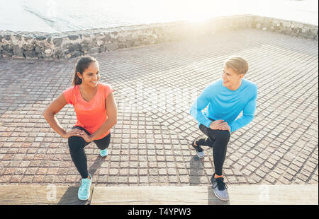 Couple Jogging stretching jambes en souriant l'un à l'autre - la formation des jeunes sportifs au coucher du soleil en plein air - Sport, relation, concept de vie Banque D'Images