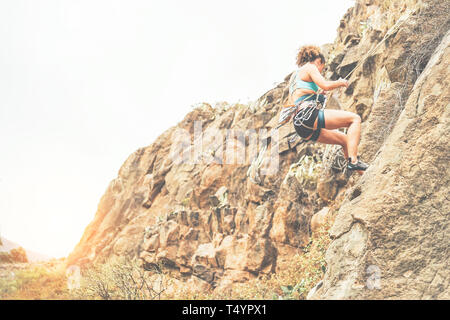 Jeune femme de grimper sur une paroi rocheuse au coucher du soleil - grimpeur sain sur la scène - Notion de haute montagne, sport extrême, de passe-temps et style de vie Banque D'Images