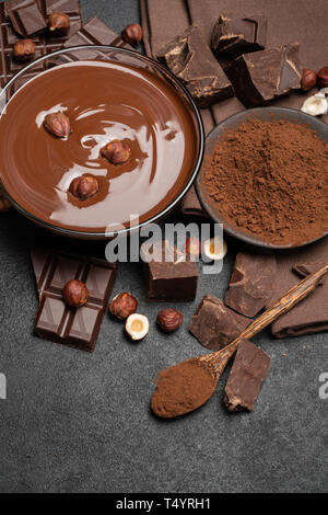 Bol en verre de crème au chocolat ou du chocolat fondu, des morceaux de chocolat et noisettes sur fond de béton foncé Banque D'Images