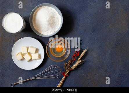 Ingrédients pour des crêpes et des crêpes sur un fond sombre. Farine, oeufs, lait, beurre, fouetter. Vue d'en haut. L'espace pour le texte. Banque D'Images