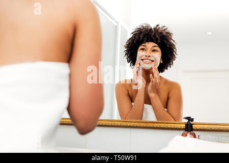 Femme souriante en appliquant la crème sur son visage naturel Banque D'Images