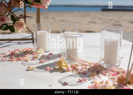 Pétales de fleurs fraîches se trouvent sur le sol près d'une arche de mariage décoration et bougies blanches. La décoration de l'événement avec des fleurs fraîches. Banque D'Images