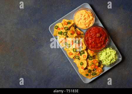 Croustilles de maïs jaune mexicaine nachos avec jalapeno, guacamole, sauce au fromage et la salsa sur fond bleu foncé Banque D'Images