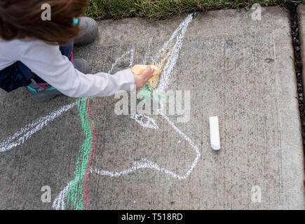 Une petite fille dessine avec des craies de trottoir sur une journée de printemps ensoleillée. Banque D'Images