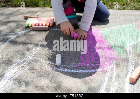 Une petite fille dessine avec des craies de trottoir sur une journée de printemps ensoleillée. Banque D'Images