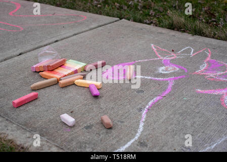 Une petite fille dessine avec des craies de trottoir sur une journée de printemps ensoleillée. Banque D'Images