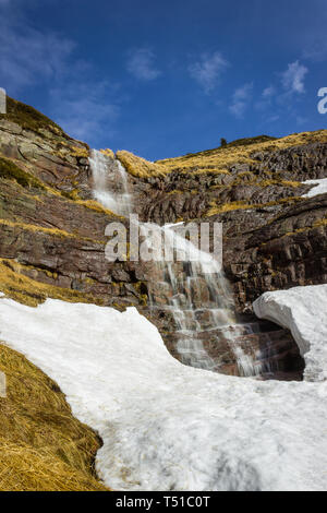 Grand scenic, belle chute d'eau tombant d'une falaise rocheuse de rouge sous la neige pendant la période de transition entre l'hiver et au printemps Banque D'Images