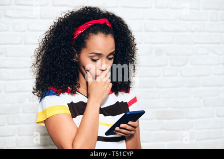 Triste african american woman reading mauvaises nouvelles sur téléphone cellulaire. Fille noire montrant la tristesse et le désespoir de message sur téléphone mobile. Personne d'origine hispanique Banque D'Images