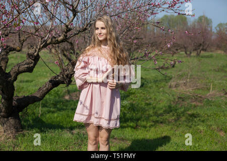 Belle blonde femme dans un jardin fleuri de pêche au printemps avec des fleurs roses Banque D'Images