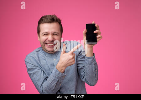 Funny jeune européen homme pointant à l'écran du téléphone de son smartphone Banque D'Images