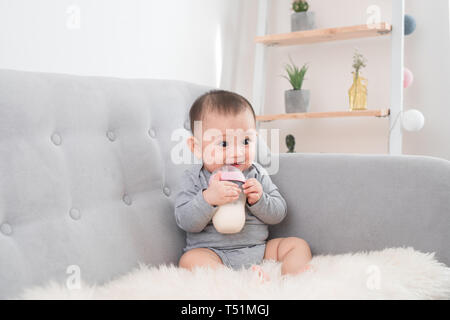 Peu cute baby girl sitting in prix sur canapé boire du lait en bouteille et souriant. Heureux l'enfant. Les concepts d'aménagement intérieur des gens de la famille. B la petite enfance Banque D'Images