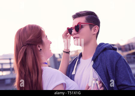 Dark-haired young guy essayant des lunettes bizarres en forme de coeur Banque D'Images