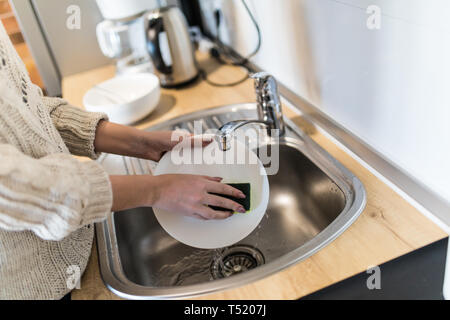 Jeune femme avec de belles mains manucure lave-vaisselle dans l'évier de la cuisine à l'aide d'une éponge avec du savon mousse . Vue en gros plan. Banque D'Images