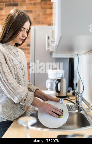 Jeune femme avec de belles mains manucure lave-vaisselle dans l'évier de la cuisine à l'aide d'une éponge avec du savon mousse . Vue en gros plan. Banque D'Images