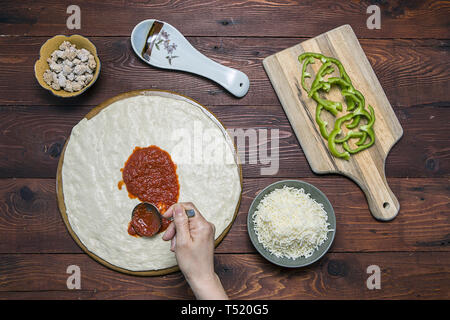 Une vue ci-dessus de propagation de la sauce à pizza sur la pâte à pizza. Banque D'Images