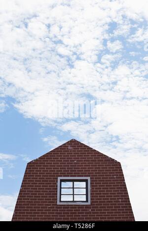 La façade d'une maison en brique, contre un ciel partiellement nuageux. Banque D'Images