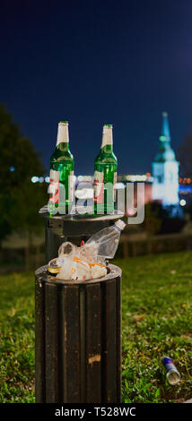 Bouteilles de bière vertes laissées dans une poubelle la nuit à Bratislava, Slovaquie, avec la cathédrale Saint-Martin floue en arrière-plan. Banque D'Images