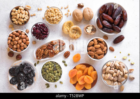 Les fruits séchés et les noix dans des bols sur fond blanc, vue du dessus. Collation santé - assortiment de fruits secs biologiques et divers écrous. Banque D'Images