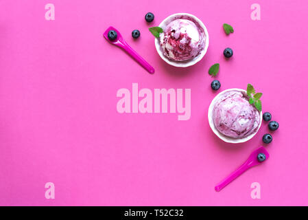 La crème glacée de bleuets sur fond rose, vue du dessus, copiez l'espace. Ecope de gelato dans cups de bleuets et de menthe. Banque D'Images
