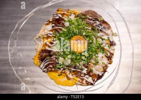 Okonomiyaki, une pizza japonaise / pancake contenant une variété d'ingrédients, sur le plateau Banque D'Images