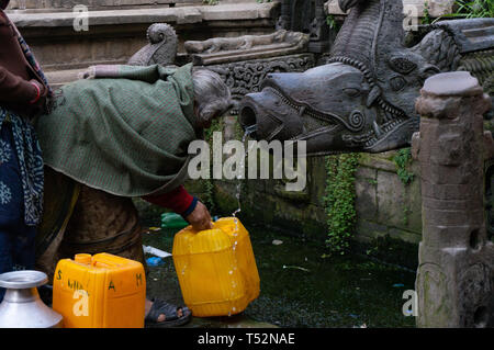 Katmandou, Népal - 28 décembre 2015 : Une vieille femme recueille l'eau du robinet en pierre historique pour l'utilisation domestique. Banque D'Images