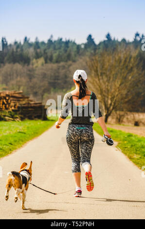 Fille courir avec le chien à l'extérieur dans la nature sur une route de forêt. Journée ensoleillée campagne coucher du soleil. Banque D'Images