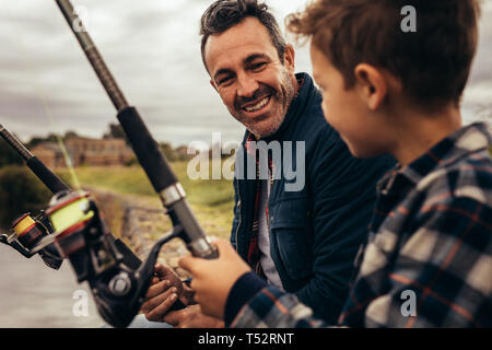 Close up de père et fils de pêche ensemble assis près d'un lac. Couple et enfant regardant à chaque autre portefeuille de pêche bénéficiant des cannes à pêche. Banque D'Images