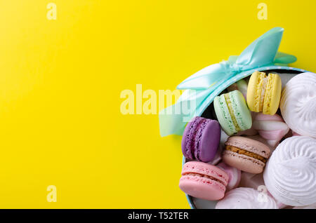 Macarons macarons multicolores ou dans une boîte turquoise avec un espace pour le texte sur fond jaune. Carte d'invitation ou de voeux concept. Banque D'Images