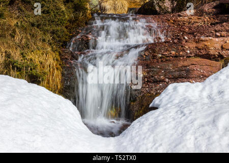 Vue rapprochée des puissants, pittoresque, belle chute d'eau tombant d'une falaise rocheuse de rouge sous la neige Banque D'Images