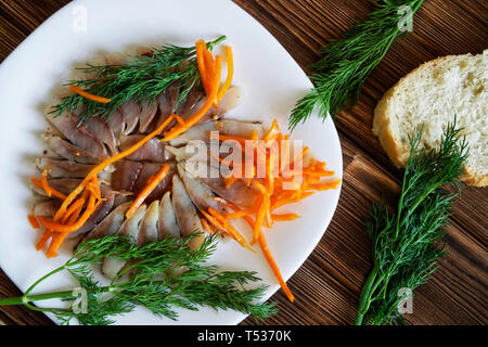 Tranches de hareng scandinave avec des épices, aneth, carottes marinées et de pain dans une assiette blanche. Réglage de la table sur une table rustique en bois essence pin boar Banque D'Images