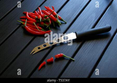 Tout en tranches et piment rouge avec un couteau à fromage et légumes crantée se situent sur une surface en bois noir. La lumière du jour. Banque D'Images