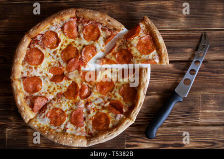Pizza au pepperoni et fromage fait maison knife se situent sur une surface en bois naturel, bois de pin. La lumière du jour. Couper une pièce. Banque D'Images