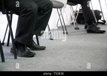 Les jambes de personnes attendant leur tour sur les chaises de bureau dans le couloir. Interview et recherche d'emploi. Responsabilités de l'emploi. Banque D'Images