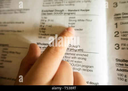 Un enfant suit recette dans un livre de cuisine et utilise ses doigts pour suivre les mots pendant qu'il lit. Banque D'Images