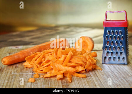 Carottes râpées se trouve dans la cuisine, sur une planche à découper en bois vintage. Rare mystère et illusion d'optique. Petits et gros Banque D'Images