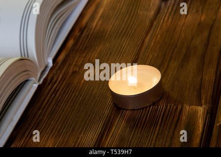 Une bougie brûlante se dresse sur planches en bois à côté d'un livre blanc ouvert à la fois de la religion et de la foi. Close-up. Banque D'Images