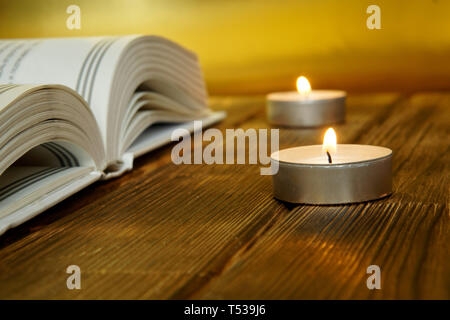 Un livre ouvert sur la religion et la foi repose sur des planches sur un fond doré. A proximité, allumé des bougies. Close-up. Banque D'Images