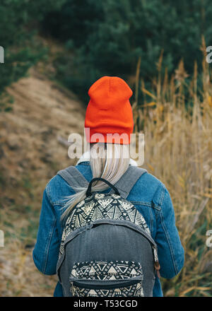 Promenade dans la nature une jeune fille dans un bonnet rouge avec un sac à dos est marcher parmi les hautes herbes sèches à l'automne Banque D'Images