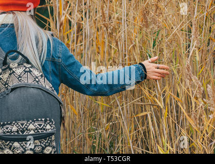 Promenade dans la nature une jeune fille dans un bonnet rouge avec un sac à dos est marcher parmi les hautes herbes sèches à l'automne Banque D'Images