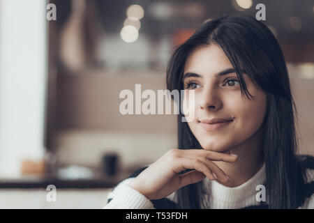 Belle woman in casual clothes smiling while sitting in cafe. Ambiance chaleureuse Banque D'Images